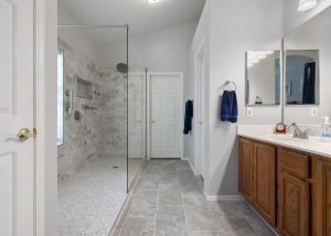 Spacious walk-in shower with floor-to-ceiling tile and glass enclosure, gray tile flooring, and wood vanity in a master bathroom remodel