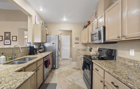 Before photo of a kitchen featuring light wood cabinets, granite countertops, stainless steel appliances, and beige tile flooring.