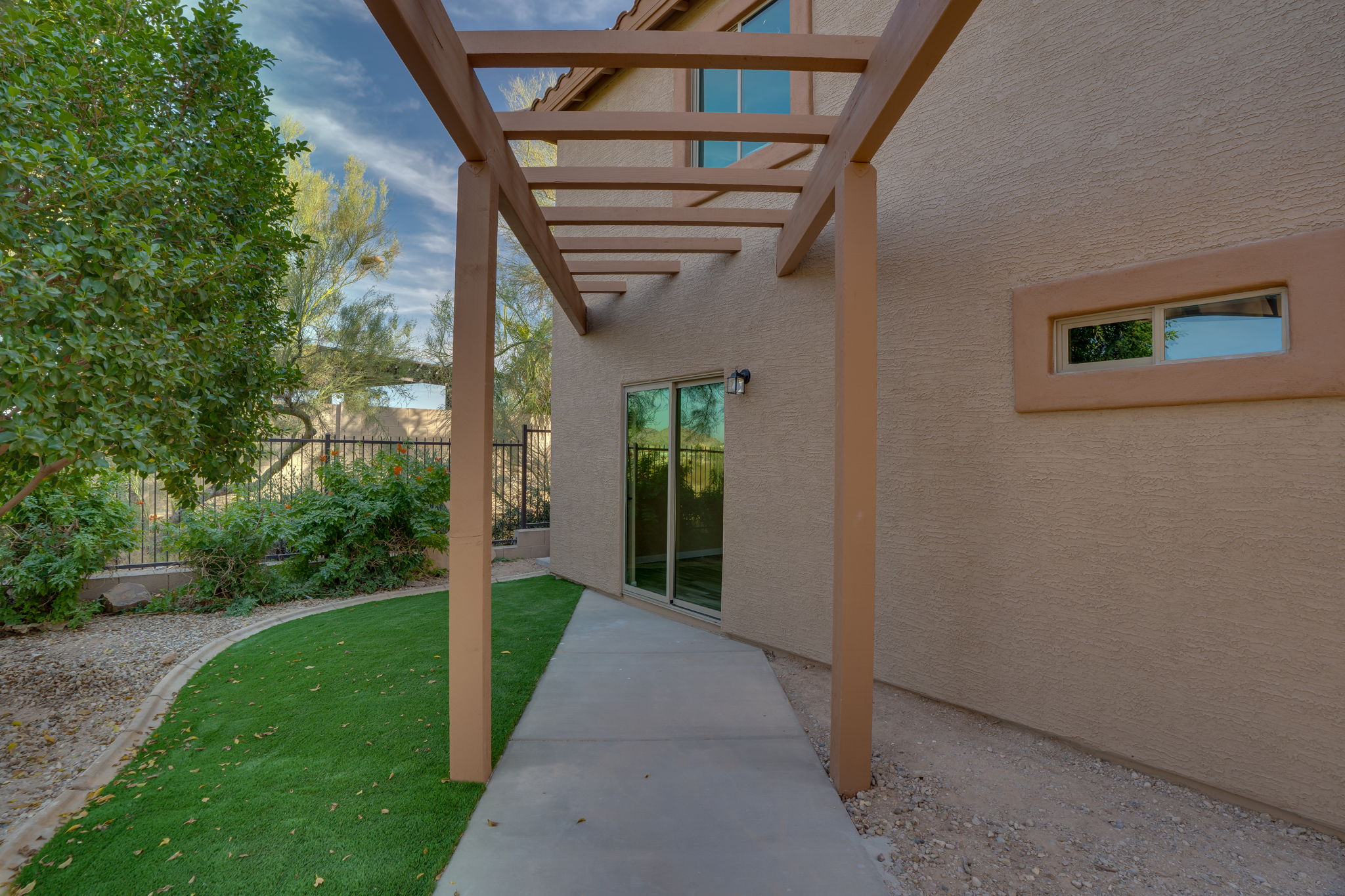 Backyard pergola leading to sliding glass doors in a two-story home.